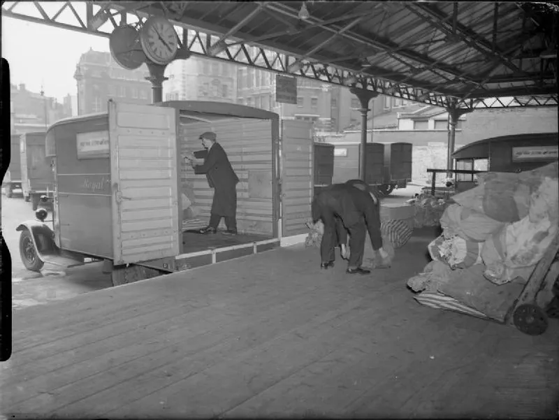 Men load sacks and bundles of mail into box vans backed up to a covered loading bay.