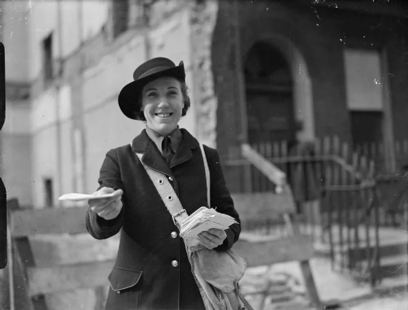 A smiling postwoman in a brimmed hat holds out a letter, with a mail bag over her shoulder and a London street behind.