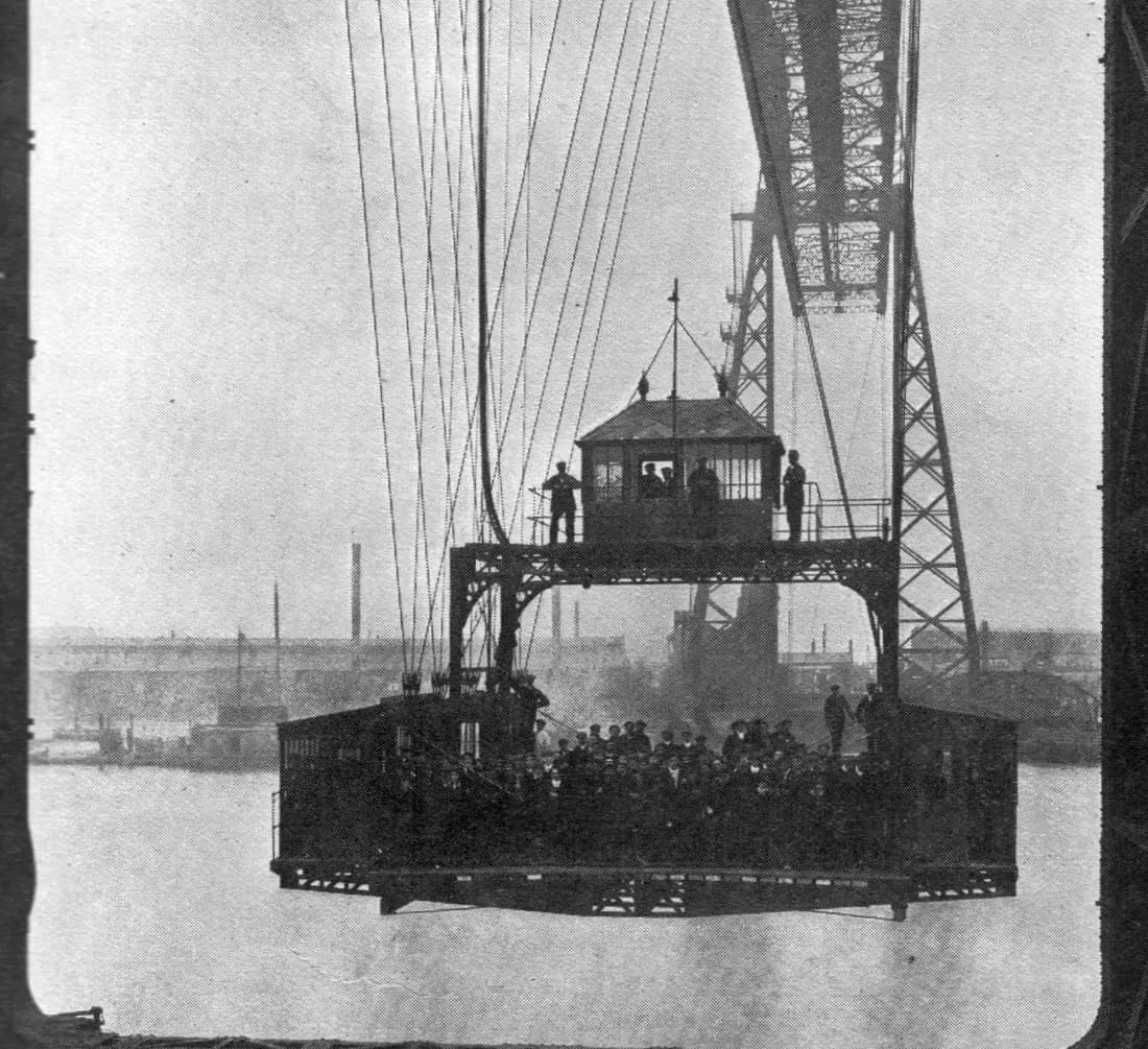 The gondola of the Transporter Bridge, packed with passengers, hangs from steel cables over the River Tees.
