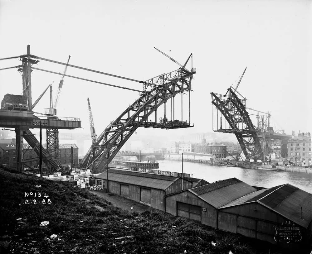 The two steel halves of the Tyne Bridge arch reach out over the river from cranes on each bank, almost meeting in the middle.